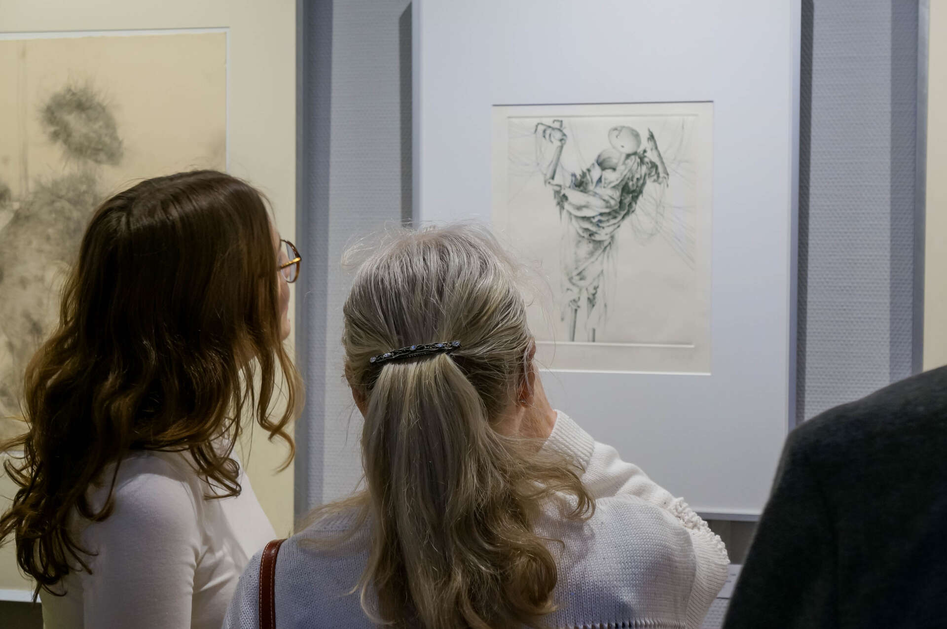 Zwei Frauen betrachten ein Bild der Ausstellung. Das Bild zeigt eine Marionette.